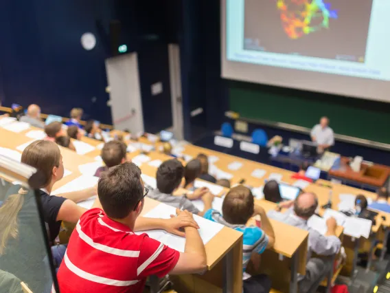 lecture room filled with students and speaker in front of screen