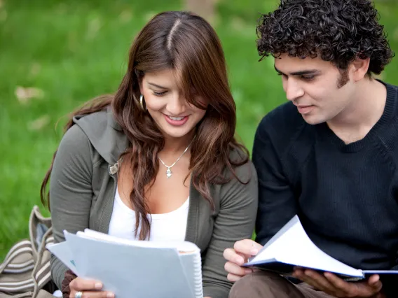 a woman and man sitting on grass looking at notebook